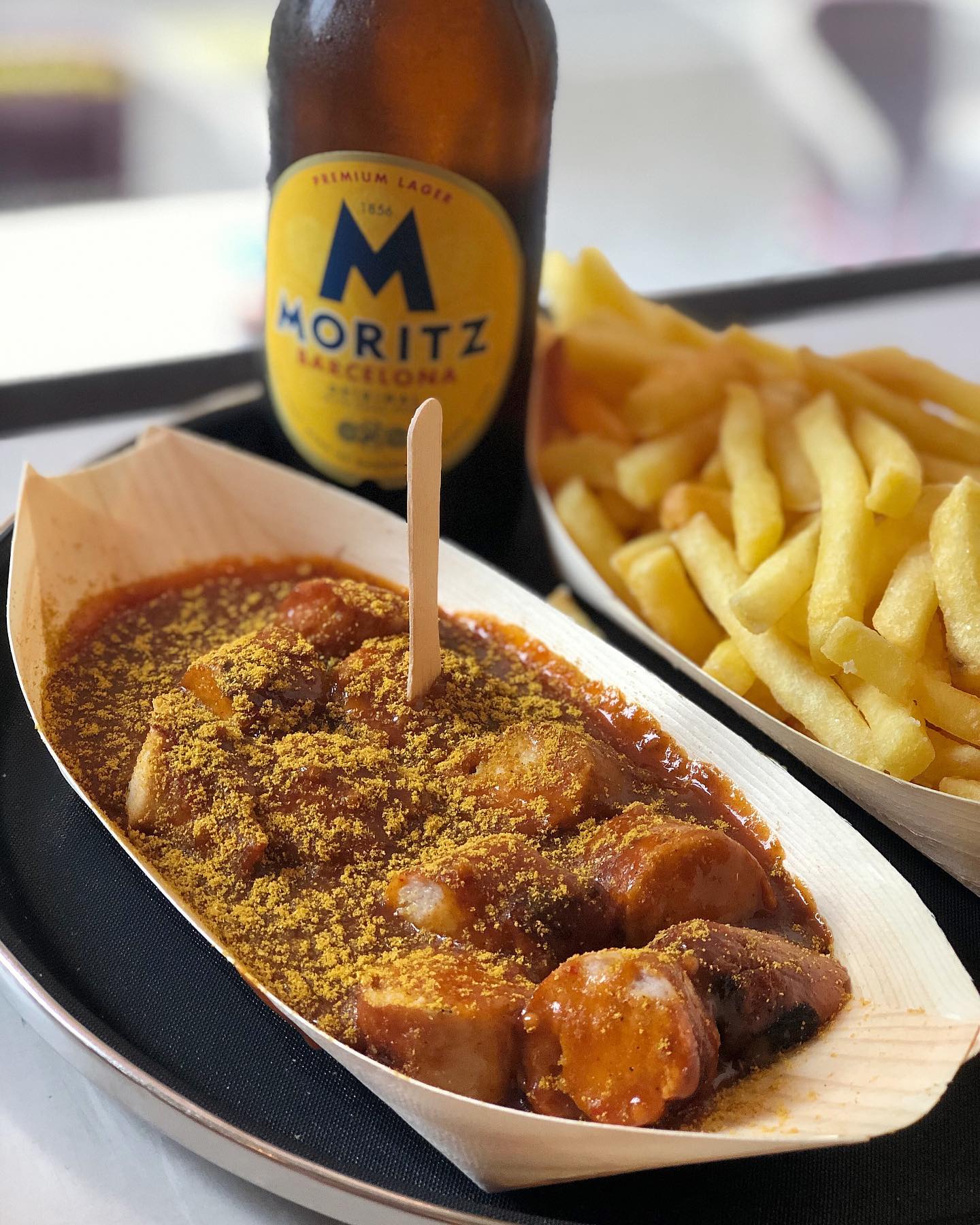 Sosej kari di atas pinggan kayu dengan kentang goreng di latar belakang.