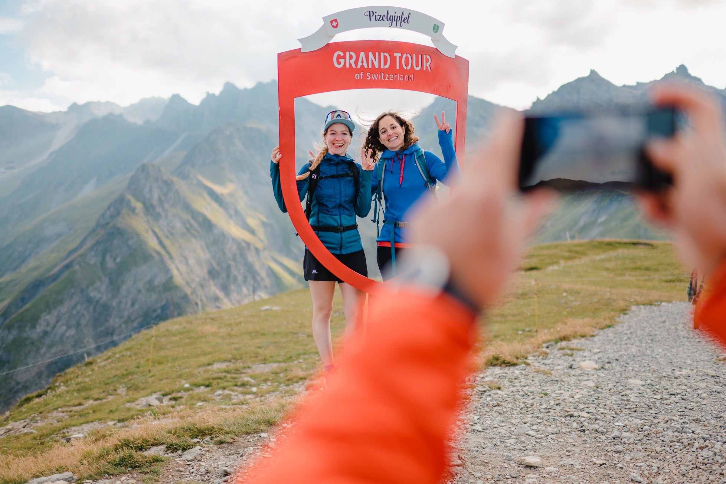جولة في سويسرا بيزول، شخصان يتجولان مبتسمين أمام منظر جبلي داخل إطار أحمر