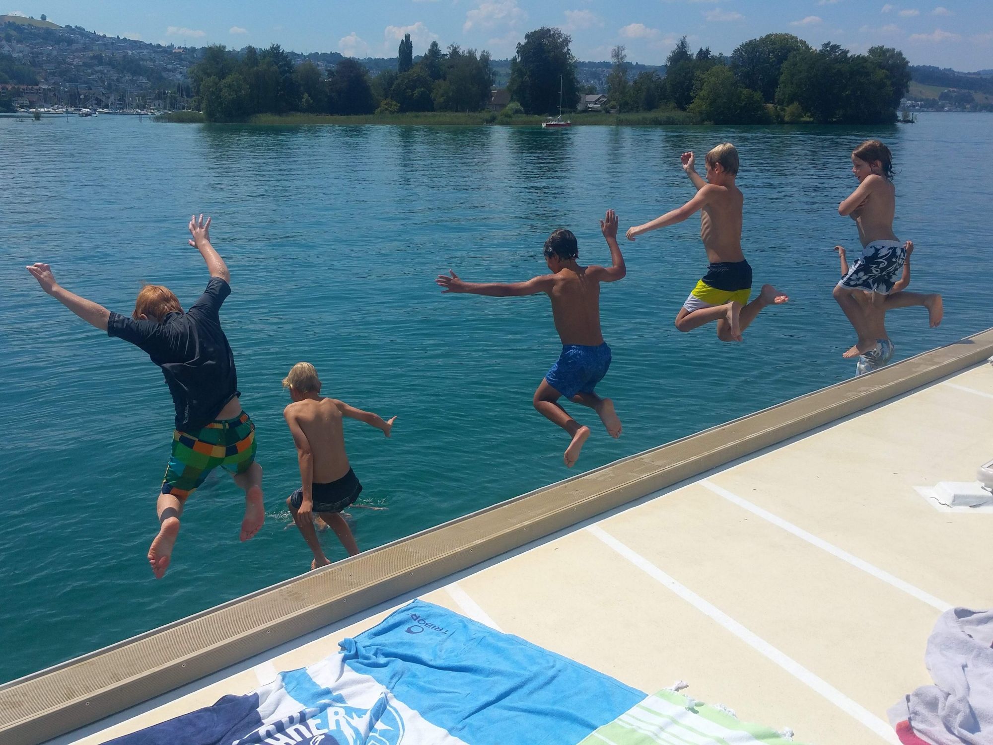 इवेंटफ्लॉस: बच्चों का समूह झील में ग्रीष्मकालीन साहसिक कार्य के दौरान पानी में कूदता है।