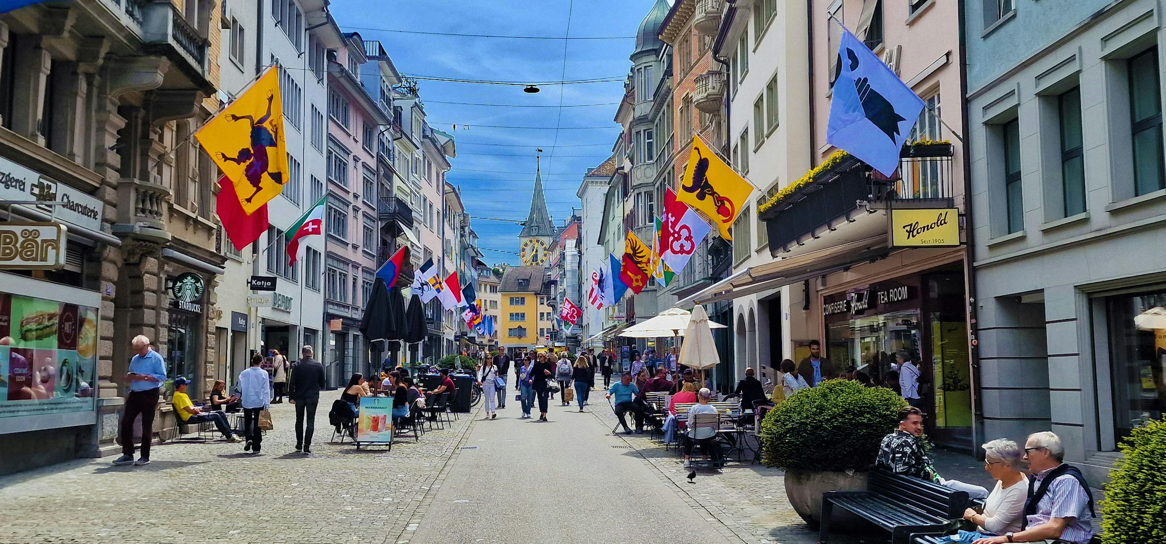 Stadtrundfahrt: Erlebe Zürich mit bunten Flaggen und lebhaften Straßencafés im Sommer.