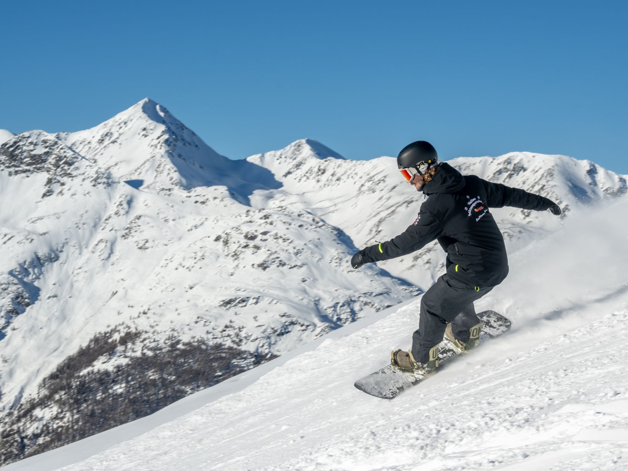 Cours de snowboard sur la Hannigalp avec de la neige et des montagnes en arrière-plan.