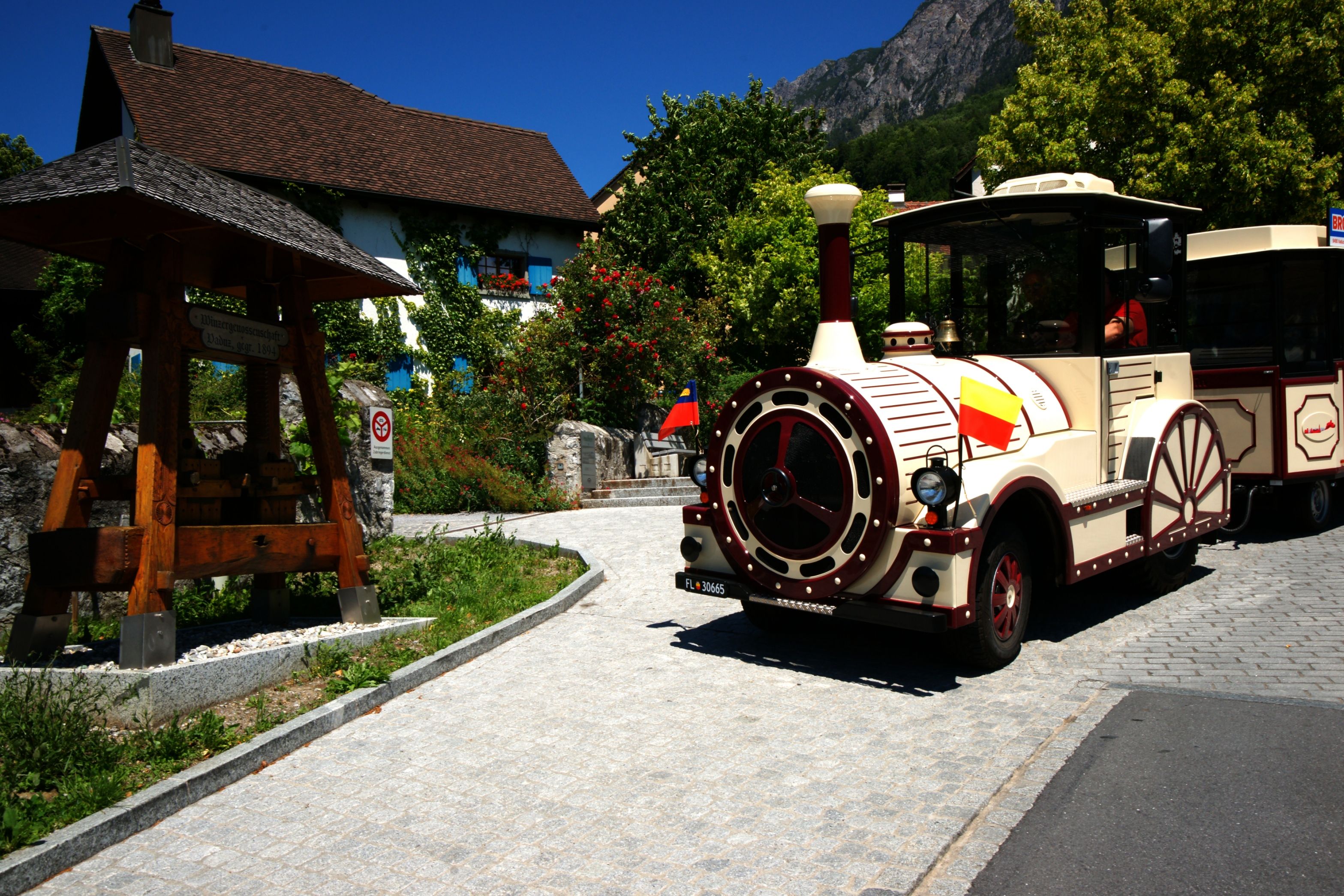 Citytrain in Vaduz fährt vorbei an malerischer Landschaft und typischen Gebäuden.