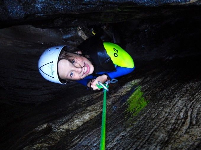 Abseiling Children Canyoning Corippo, smiling child with helmet moves along rope next to rock face
