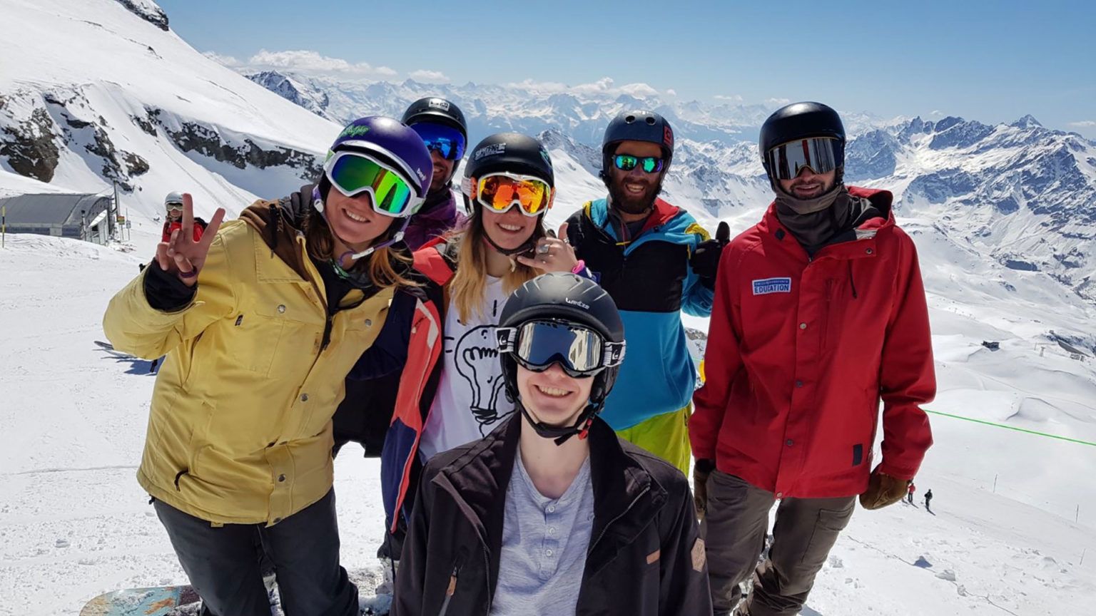 Scuola di sci: gruppo di sciatori e snowboarder in montagna con sole.