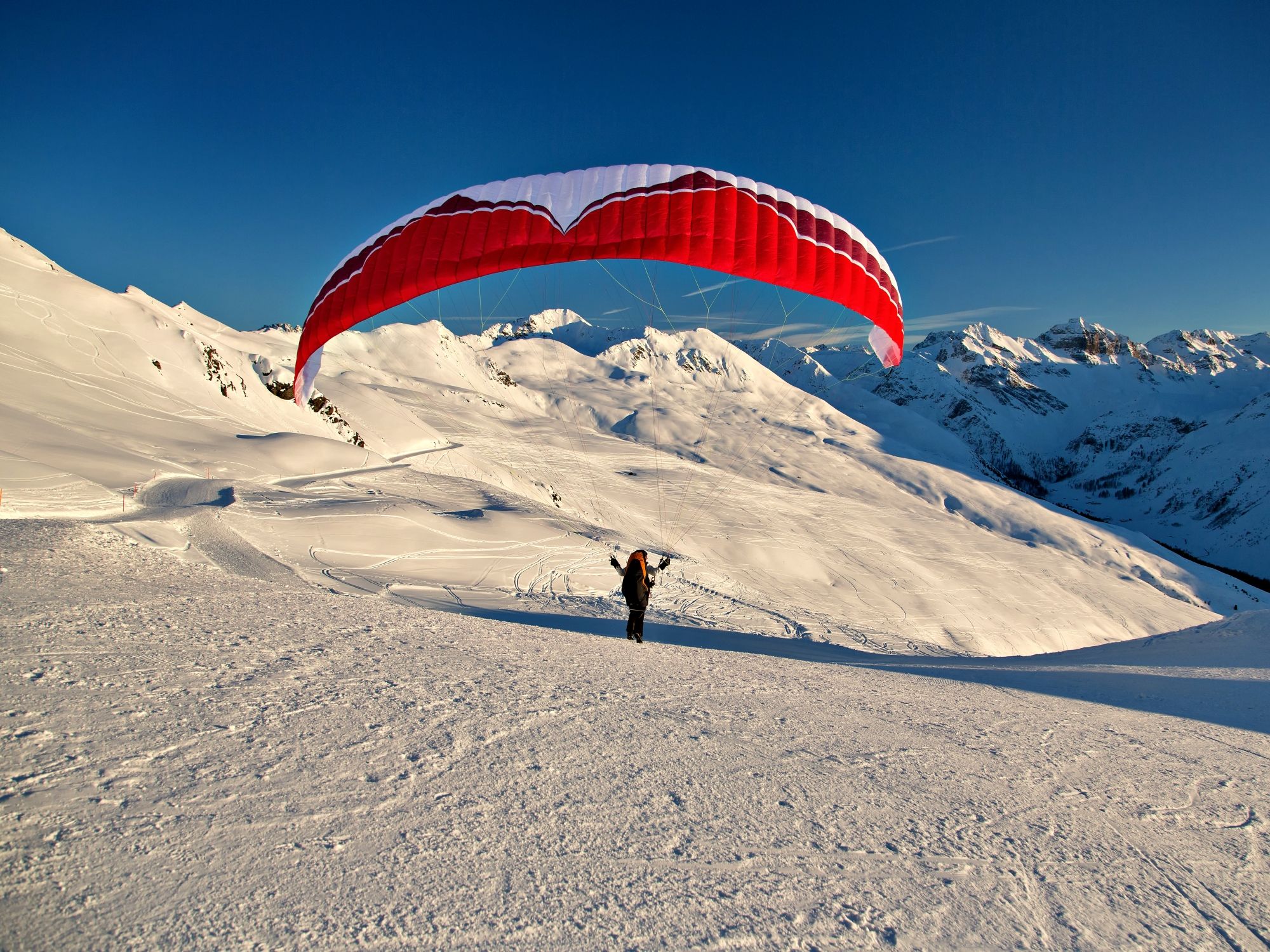 Paragliden in Klosters met rode parachute, sneeuw, berglandschap.