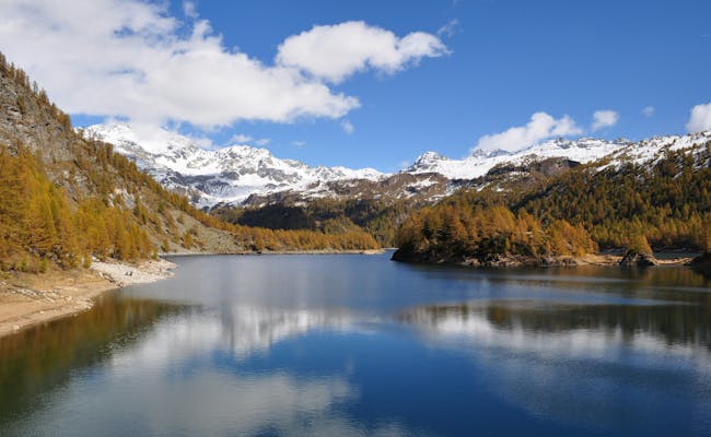 Alpe Devero: Reflexión del cielo en el claro lago rodeado de paisajes montañosos otoñales