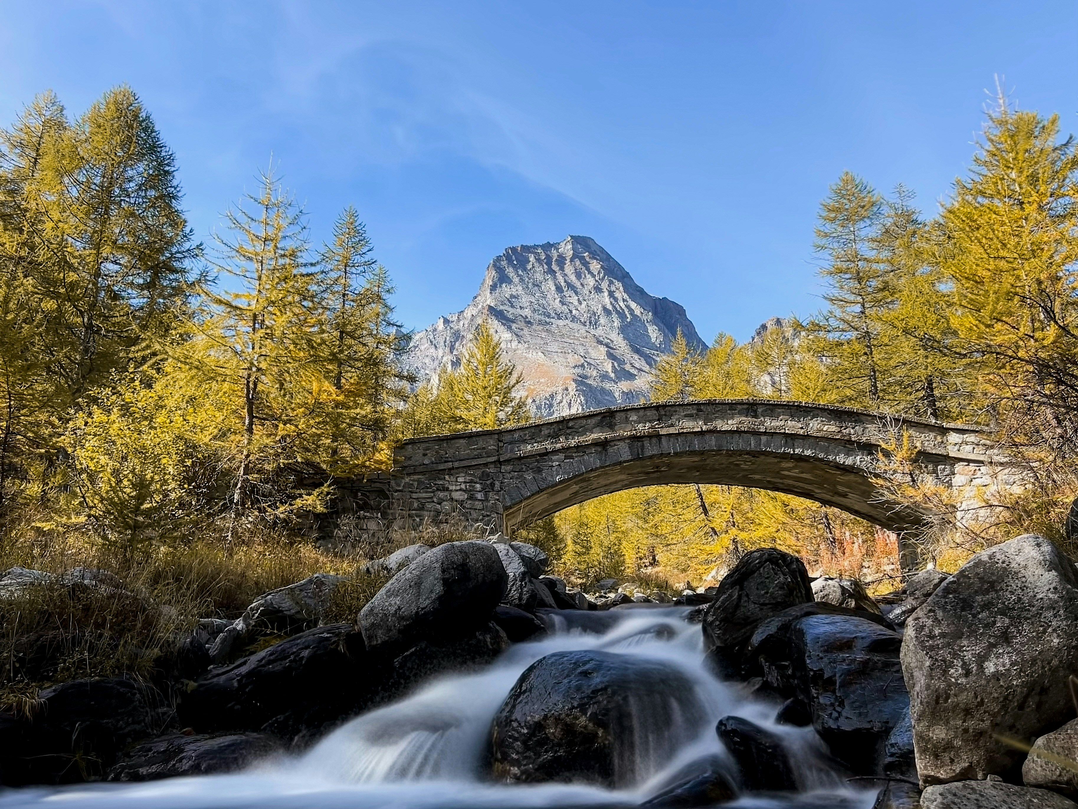 Alpe Veglio: ทิวทัศน์ภูเขาที่น่าประทับใจกับแม่น้ำ, สะพานหิน และป่าใบไม้เปลี่ยนสีในฤดูใบไม้ร่วง.