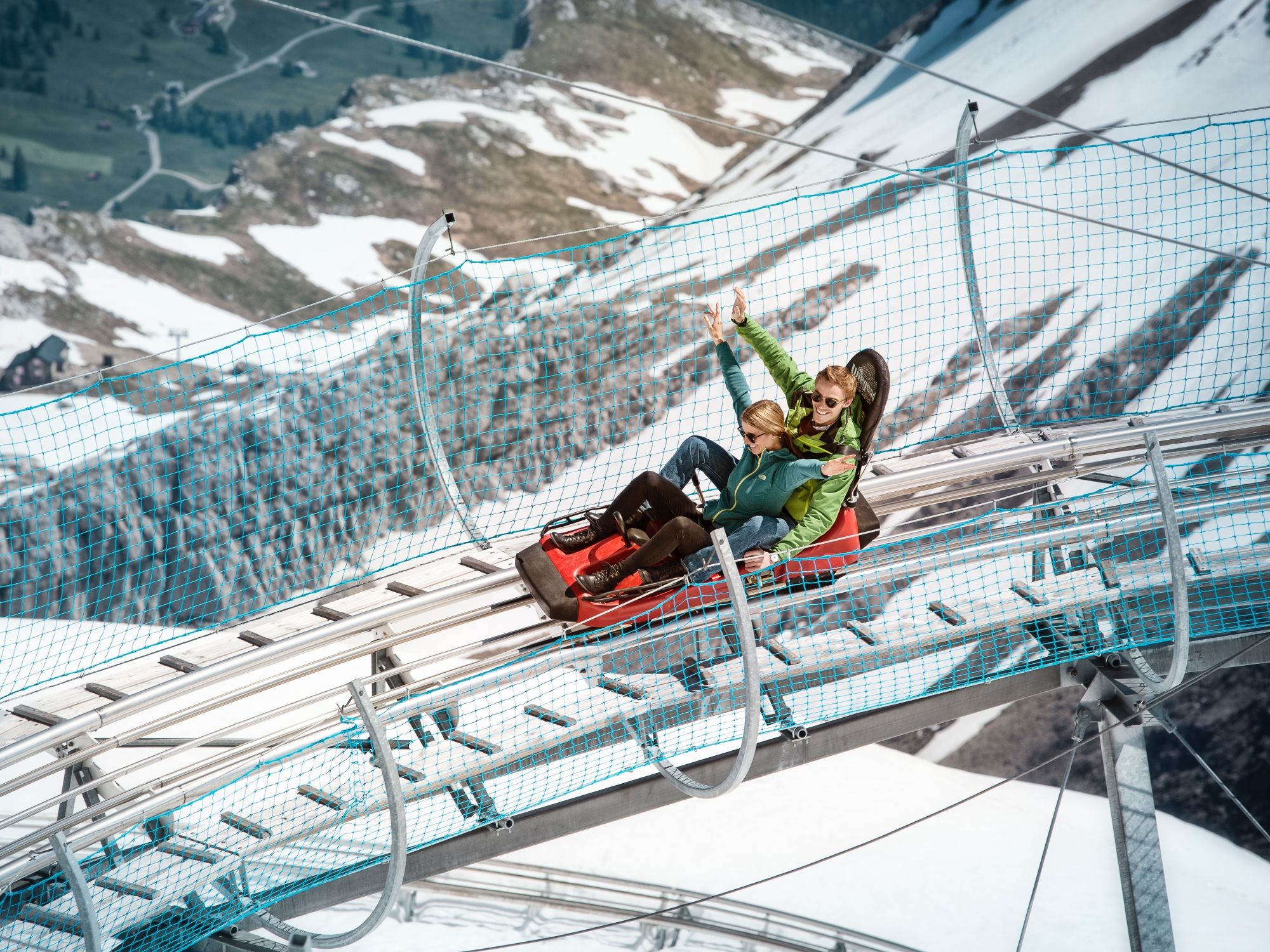 스키 리프트를 타고 있는 산악 코스터 글래시어 3000과 녹색 재킷을 입은 탑승객들, 눈 덮인 풍경 위에 있습니다.