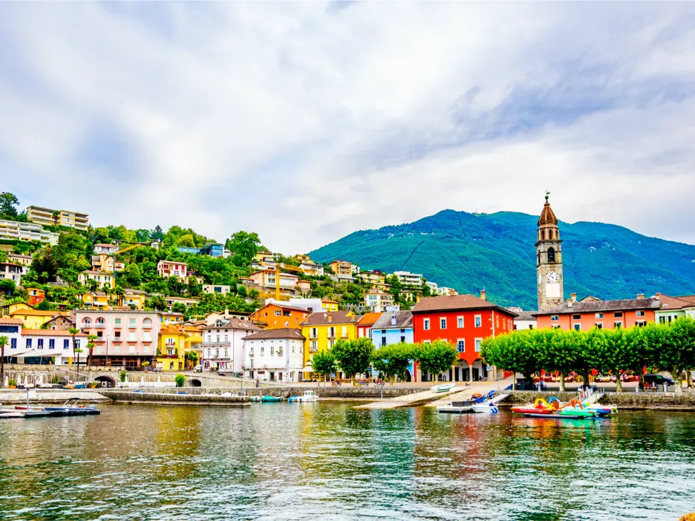 Vista cittadina di Ascona con case colorate al porto, Lago Maggiore, giornata soleggiata.