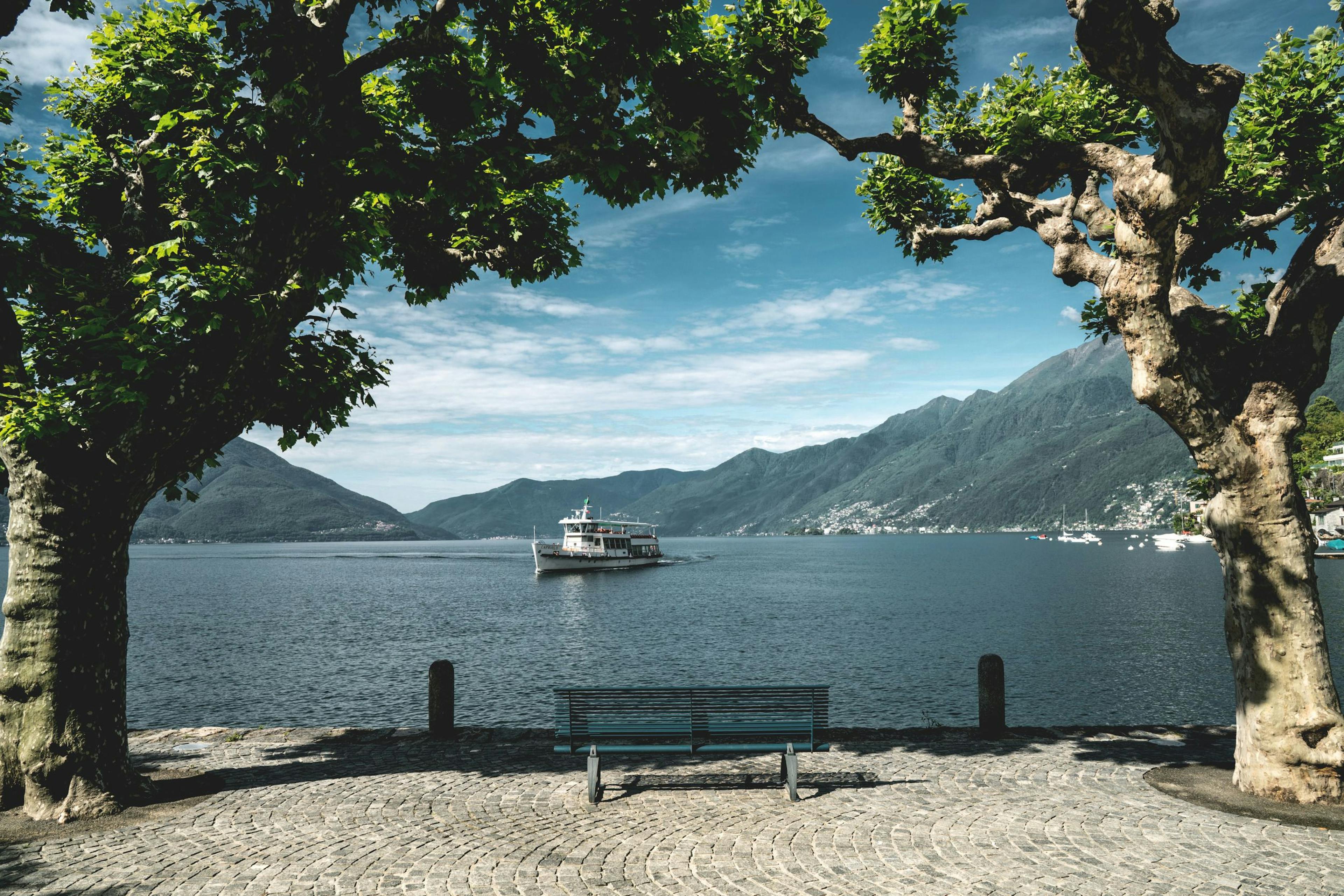 Ascona: malerische waterfront mit boot und bergen, ideal für entspannende spaziergänge am see.