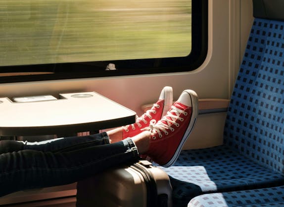 Treinreis: Ontspannen instelling met rode sneakers in de trein tijdens een zomertocht door het landschap.