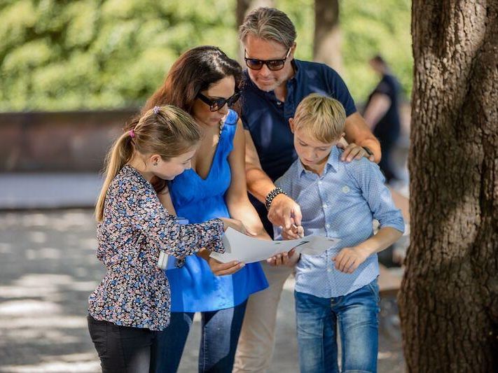 Familie betrachtet Karte bei selbstgeführter Tour in Basel. Sonne scheint. Kinder und Erwachsene erkunden die Stadt.