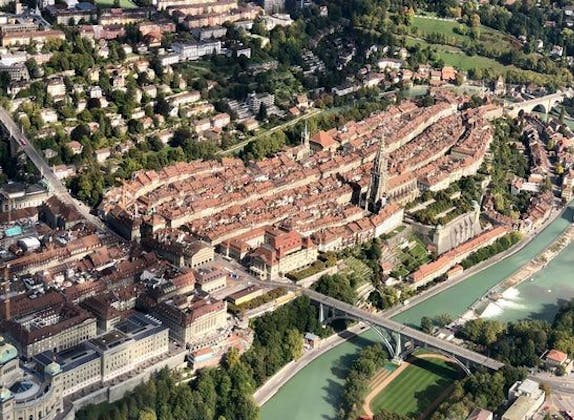 Vue aérienne de la vieille ville de Berne montrant des bâtiments historiques, une rivière et une verdure environnante.