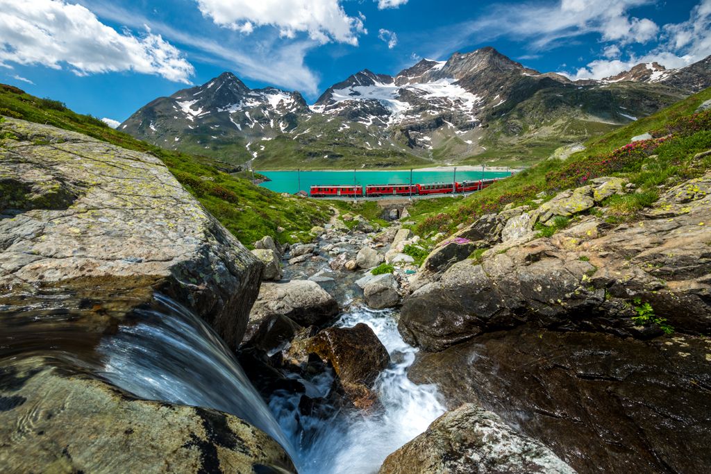 Bernina Express at Lake Bianco: Train ride through the alpine landscape of Engadin in summer.