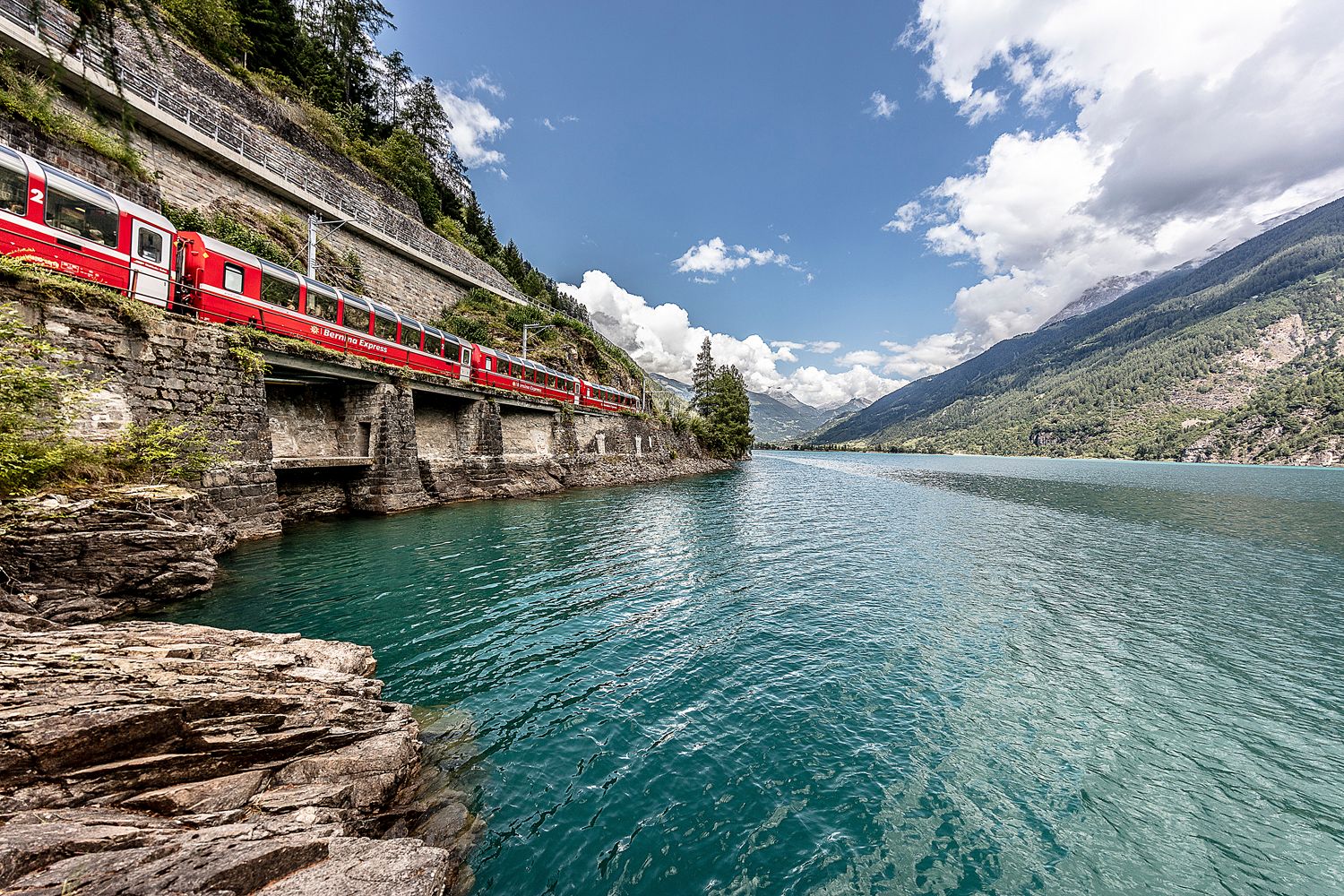 Bernina Express: Eindrucksvoller Zug entlang des grünen Stausees in den Bergen der Schweiz.