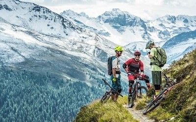 Mountain biking in the Upper Engadin, bikers standing on a trail, mountains in the background.