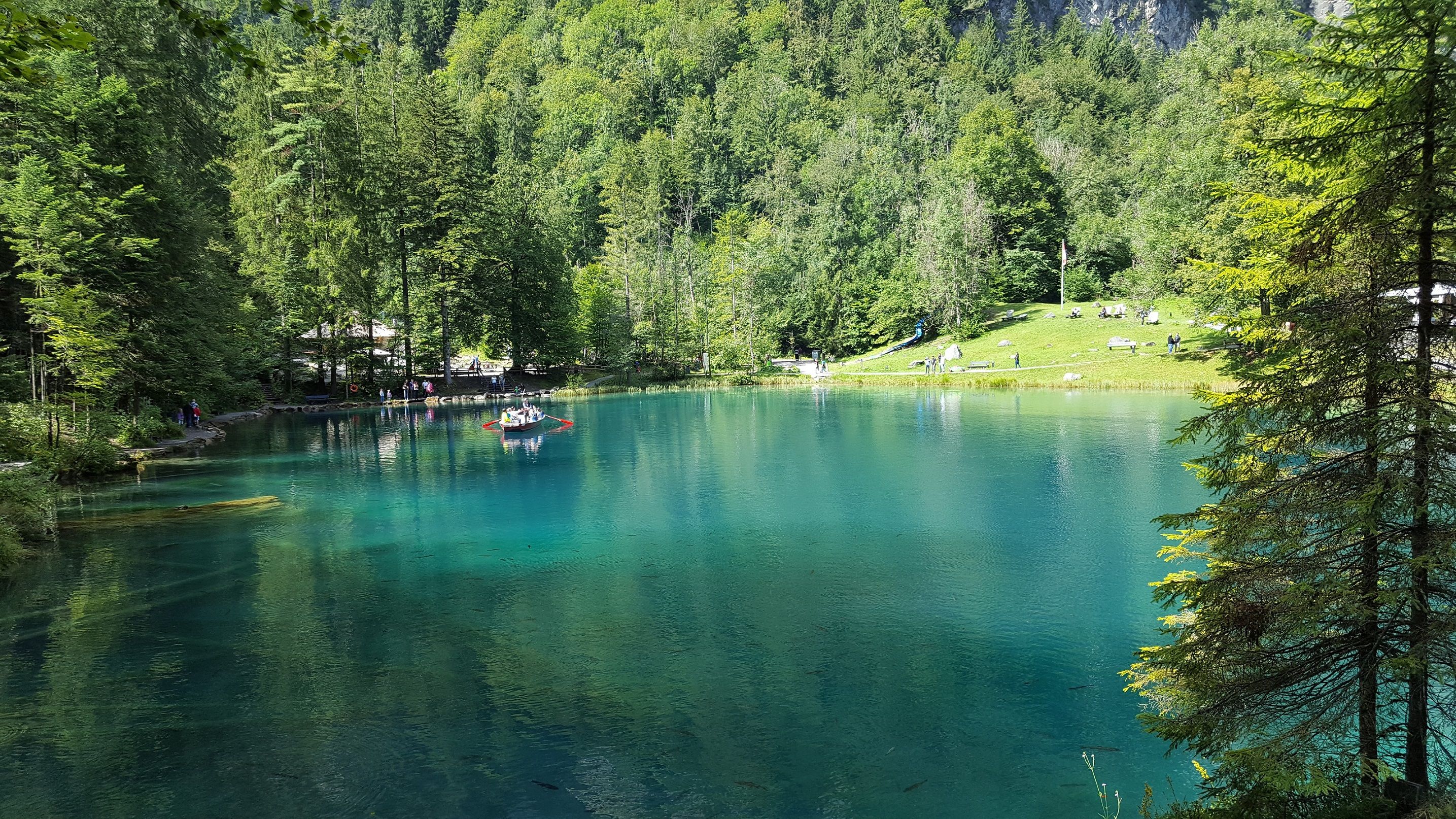 Bláhusové jezero s člunem na čisté vodě, obklopené lesem a horami v létě