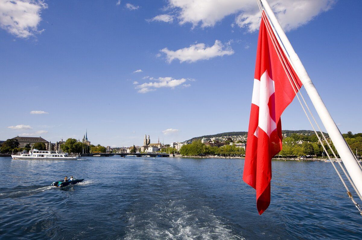 Bootsfahrt auf dem Vierwaldstättersee mit Sicht auf Ufer und Schweizer Flagge.