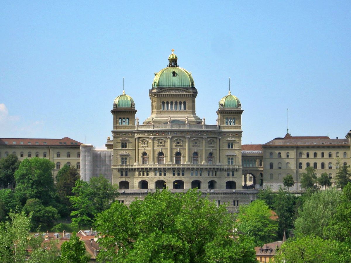 Bundesparlamentet i Bern framför en grön bakgrund, klar himmel och arkitektoniska detaljer tydligt synliga.