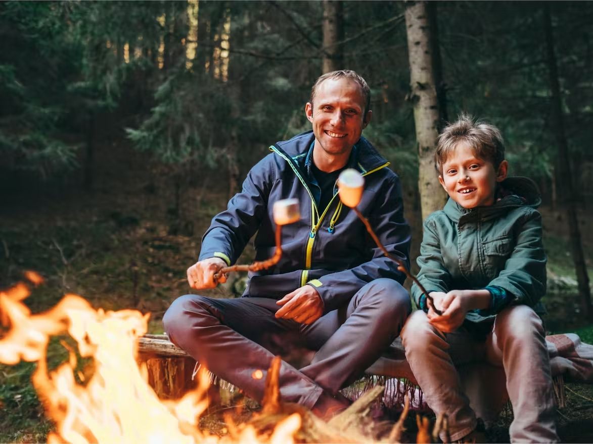 استئجار معدات التخييم: أب وابنه أمام نار المخيم، يشوي المارشميلو.