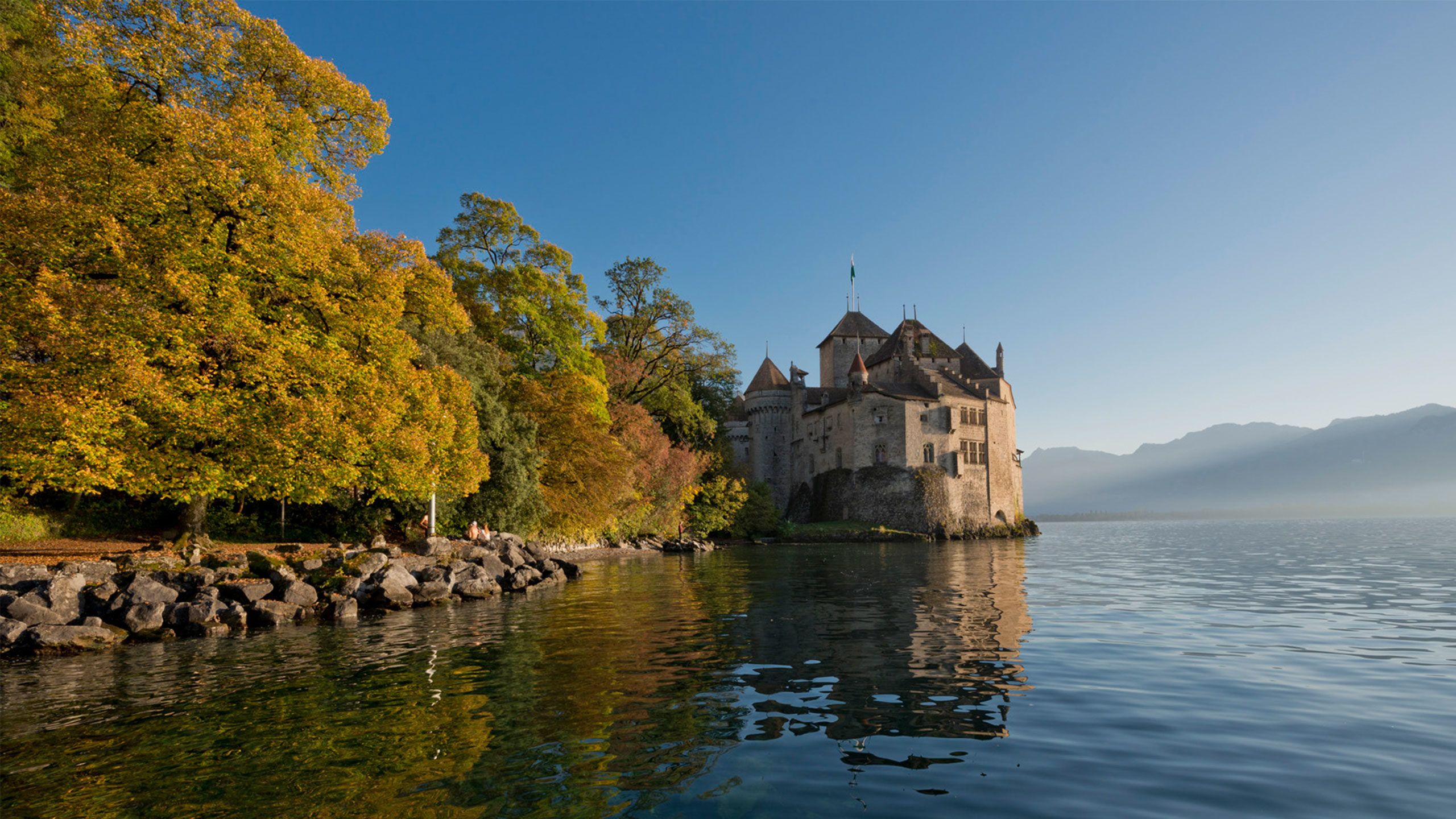 Chateau Chillon di tasik Geneva dengan pokok musim luruh yang berwarna-warni dan air yang tenang.