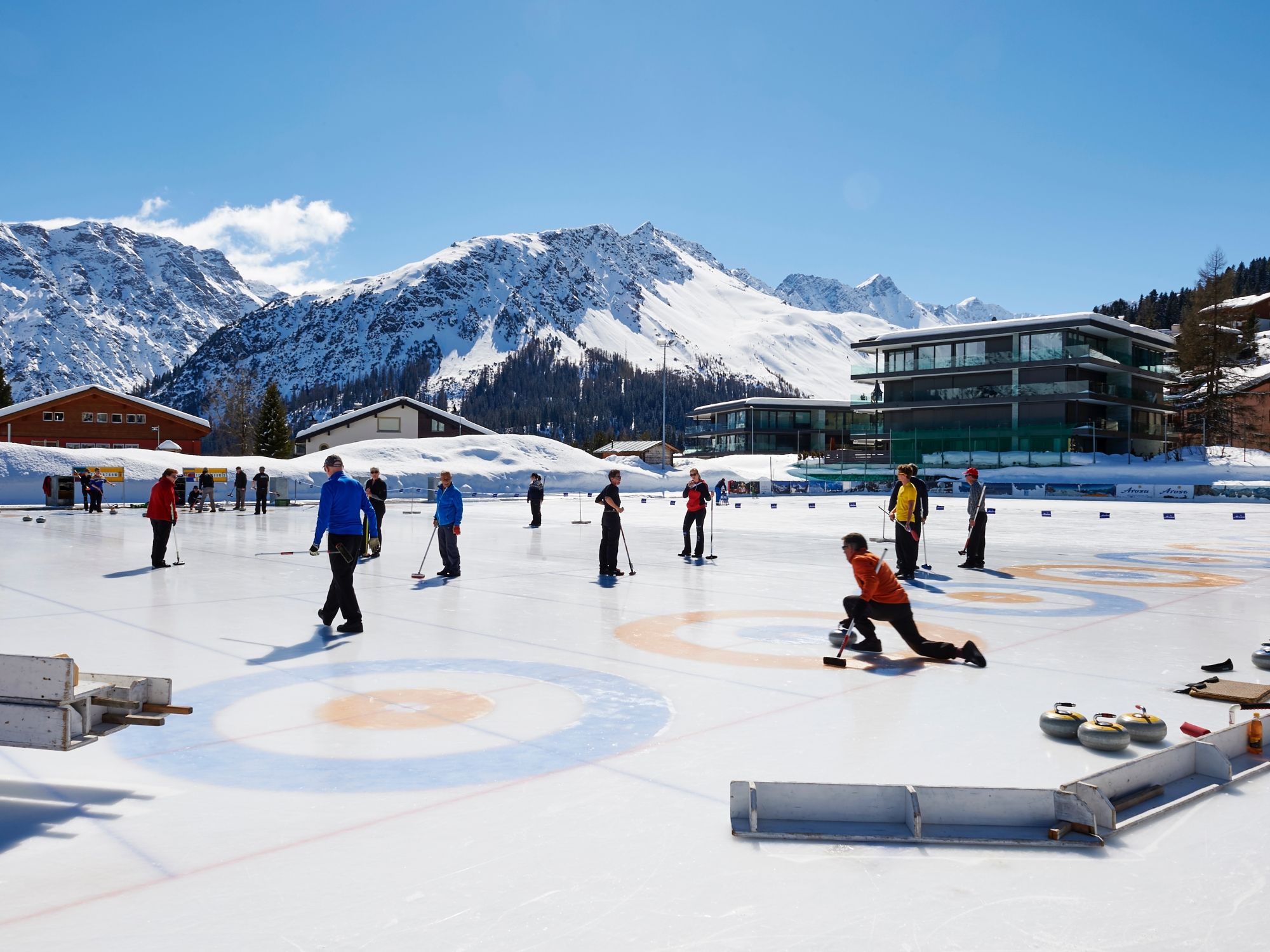 Szkolenie z curlingu w Arosie z uczestnikami na lodowisku i w zimowym krajobrazie.