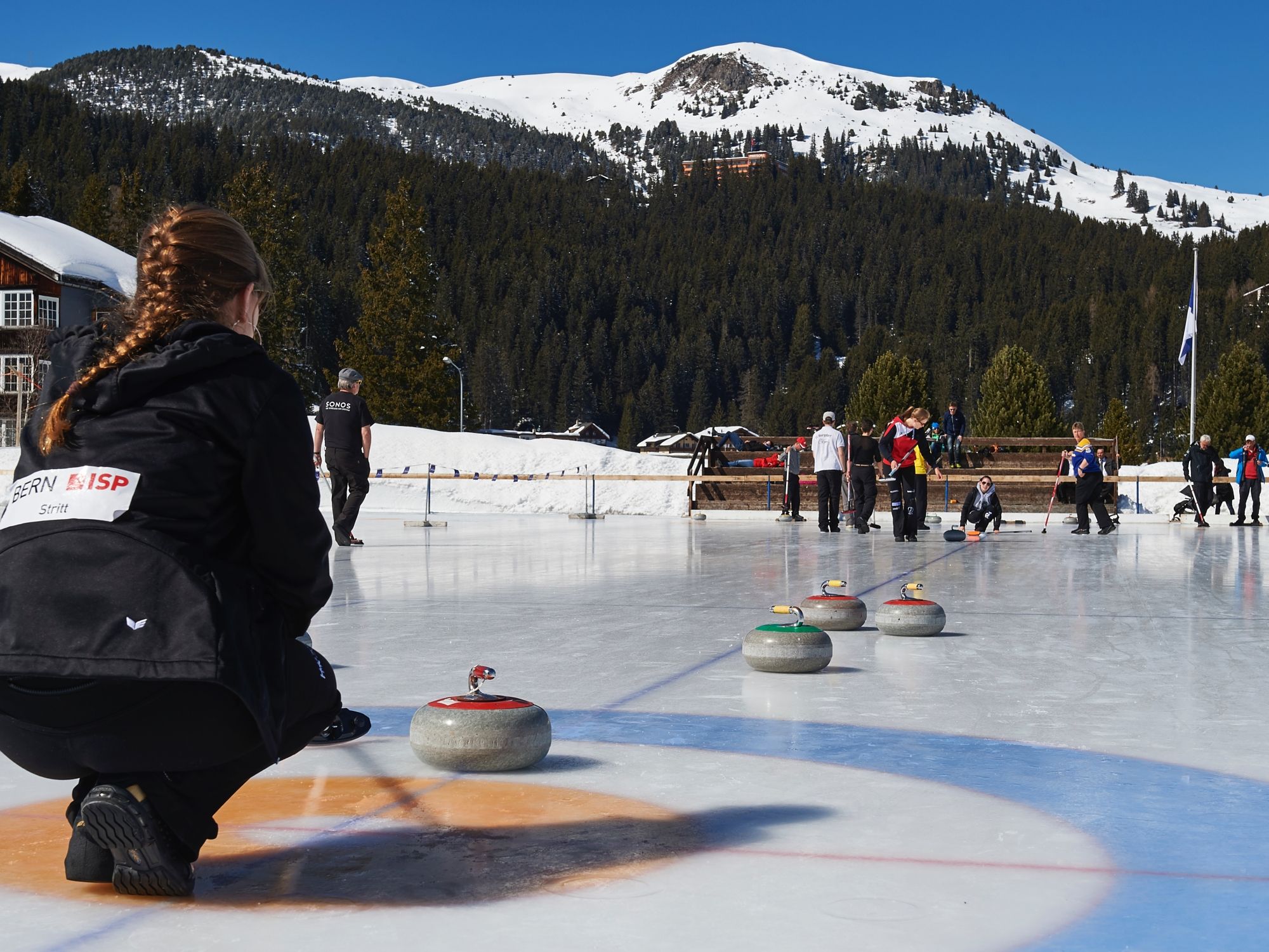 Szkolenie z curling na Arose z uczestnikami na lodzie i zasypanych śniegiem górach.