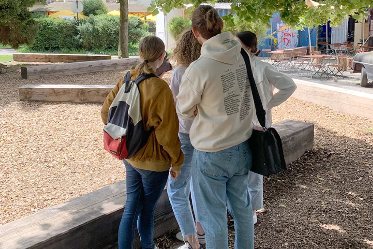 Inside Winterthur: Gruppe erkundet einen schönen Ort in der Stadt, umgeben von Bäumen und Sitzgelegenheiten.