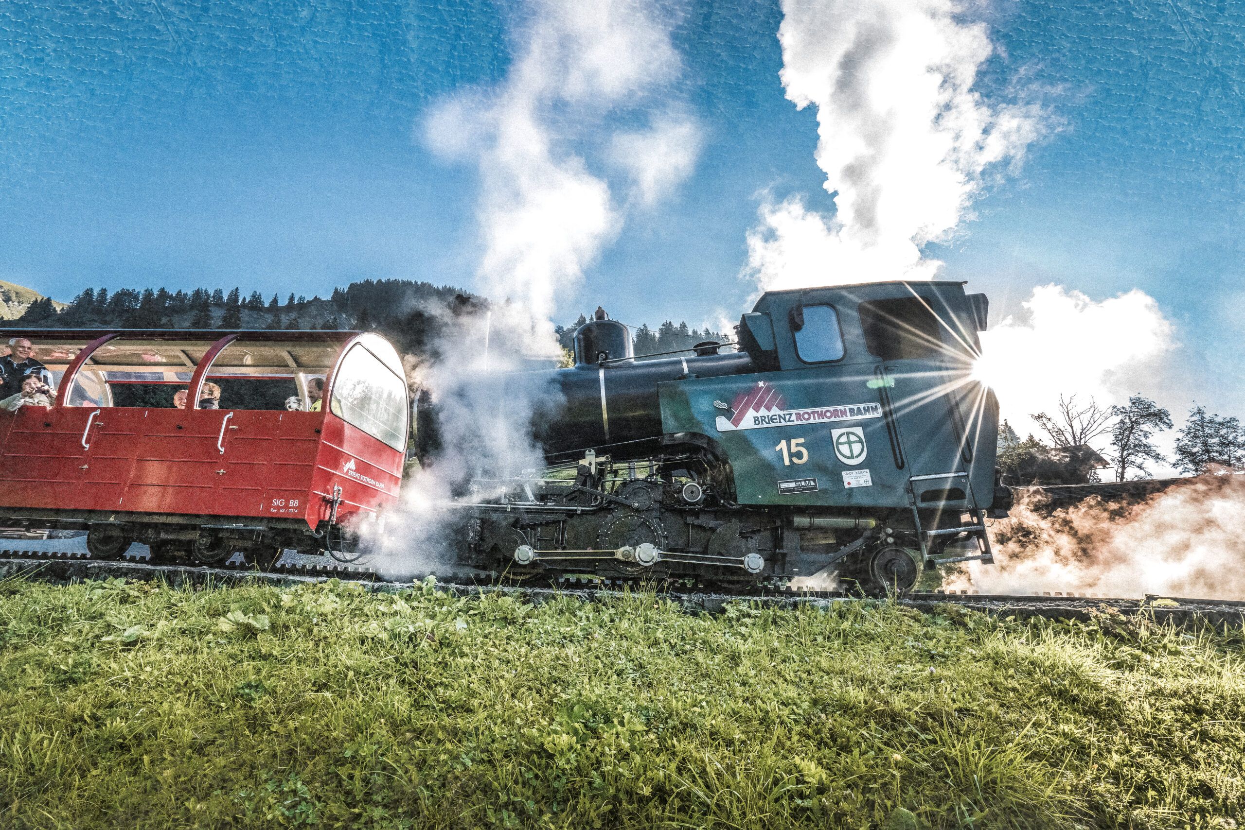 Locomotiva a vapore della Rothorn Bahn passa con carrozza panoramica attraverso il paesaggio alpino.