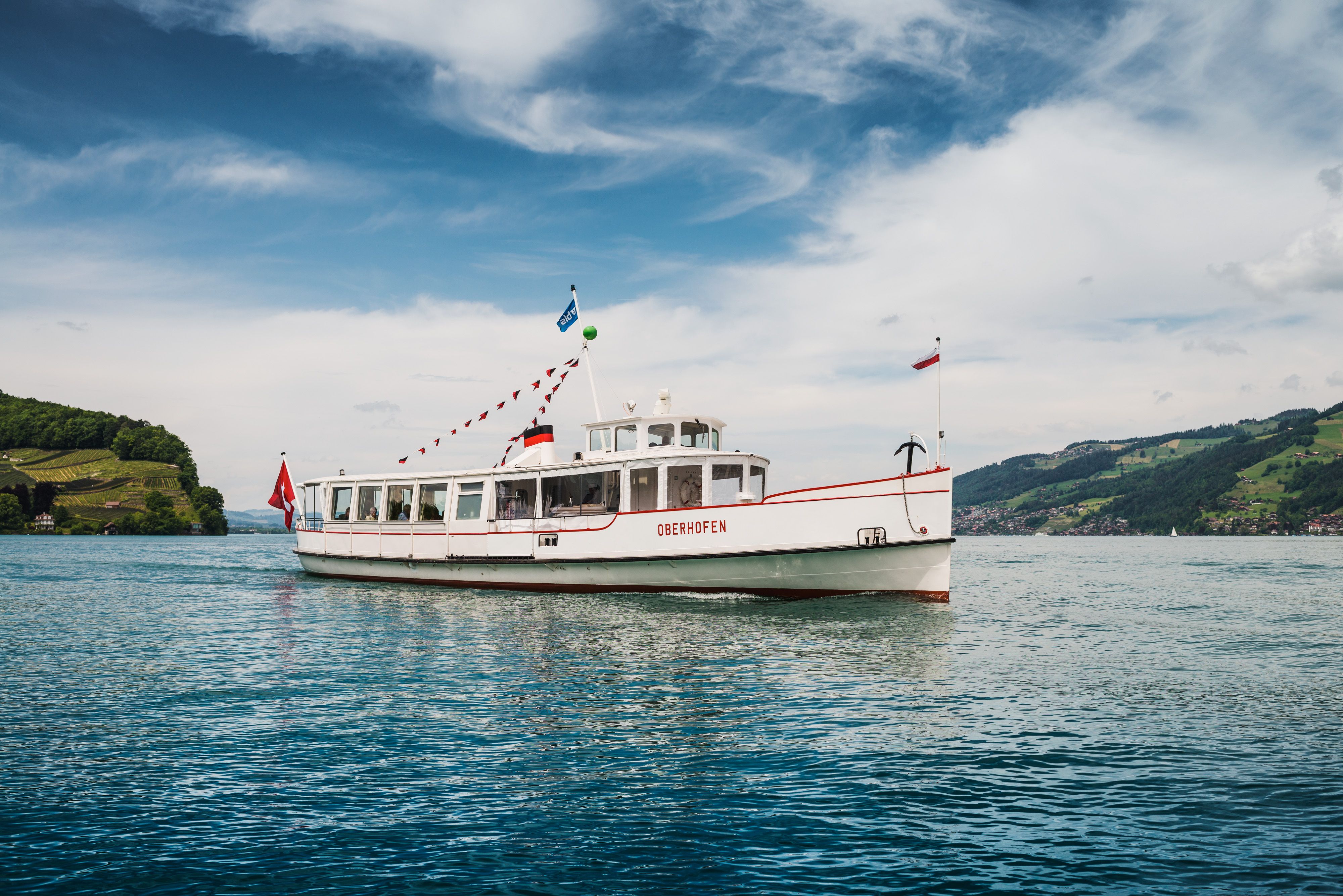 Dampfschiff Brienzersee fährt über den Thunersee, umgeben von grüner Landschaft. Wasserspiegelung sichtbar.