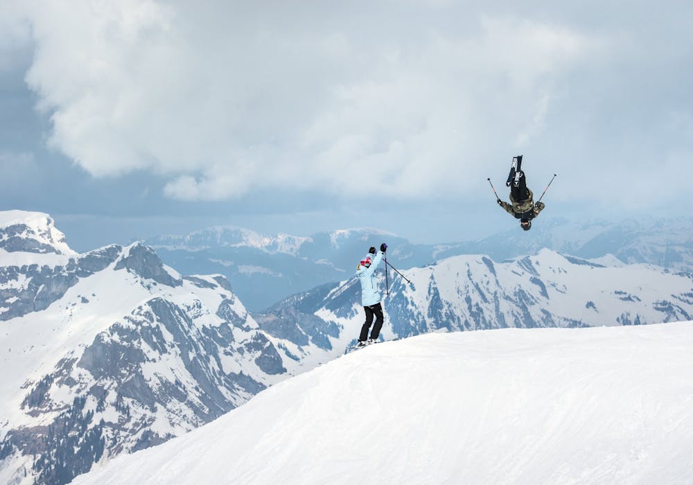 Engelberg Freeride mit Skifahrer in der Luft, Berglandschaft im Hintergrund, winterliche Bedingungen.