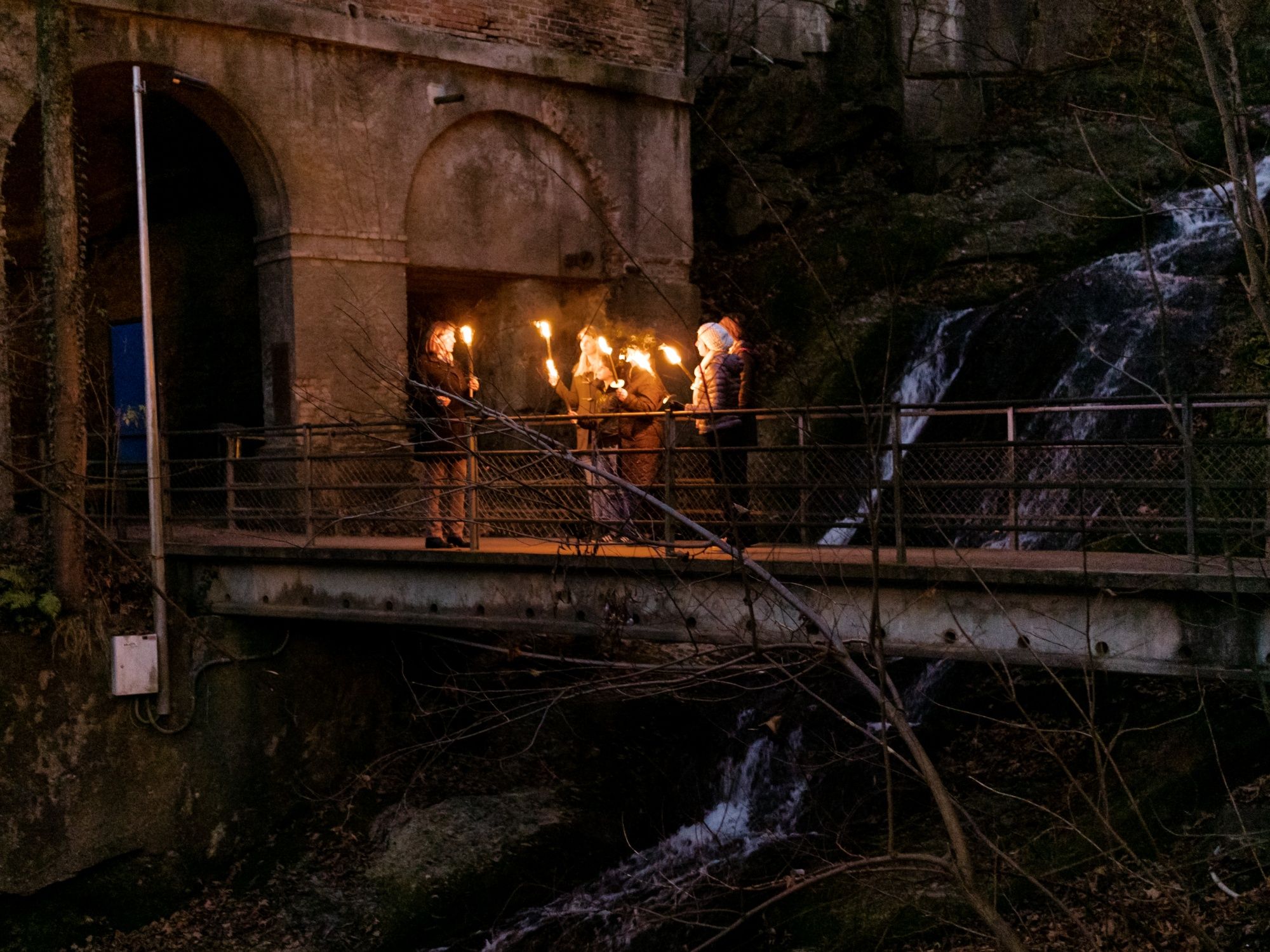 Panduan obor di Ngarai Mühlen dengan obor menyala dan air terjun di latar belakang.