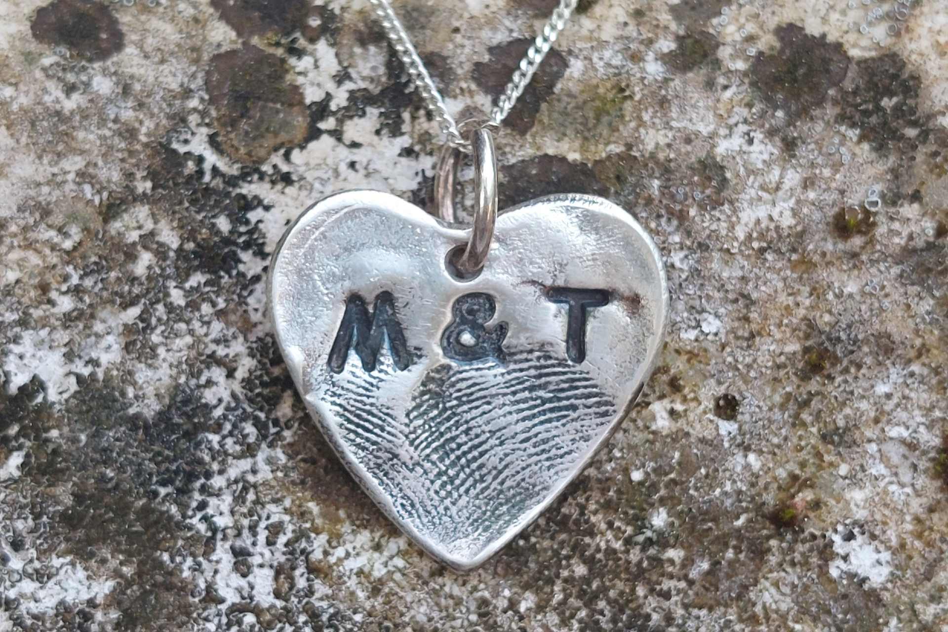 Pendentif en argent en forme de cœur avec des initiales, symbolise l'amour et la famille, parfait pour des occasions spéciales.