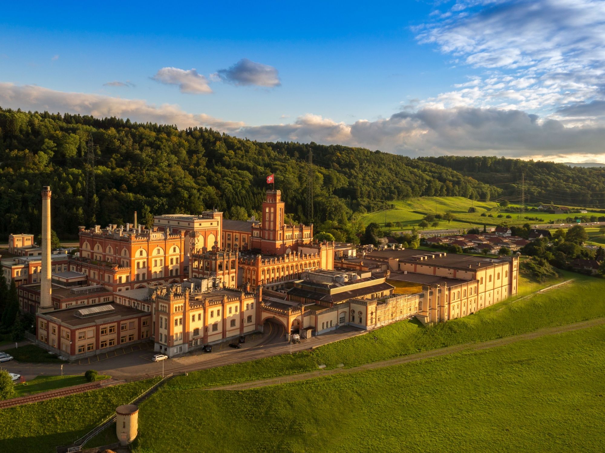 Pabrik Bir Feldschloesschen di alam, dikelilingi oleh area hijau dan bukit berhutan.