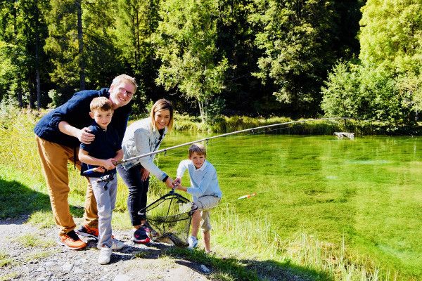 Keluarga sedang memancing di danau trout pada tahun 2023, hari cerah, lingkungan hijau.