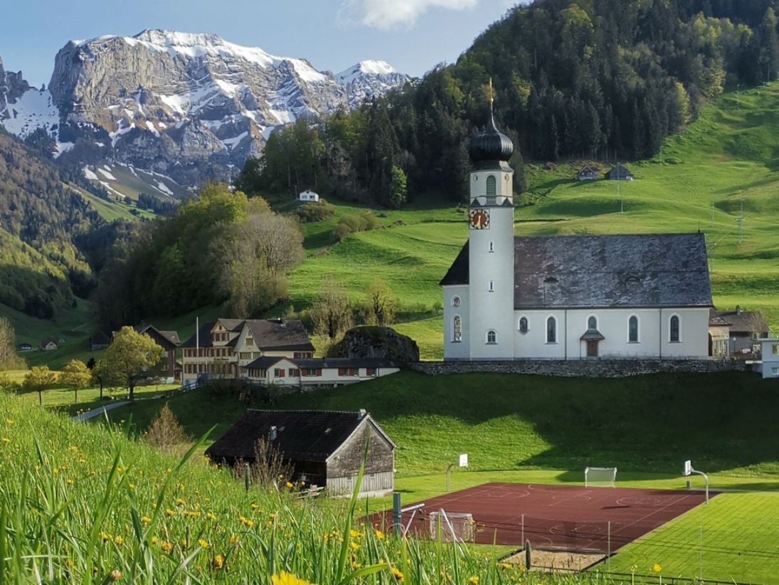 Fattoria Heidi in Svizzera: paesaggio idilliaco con chiesa, prati verdi e montagne in Svizzera.