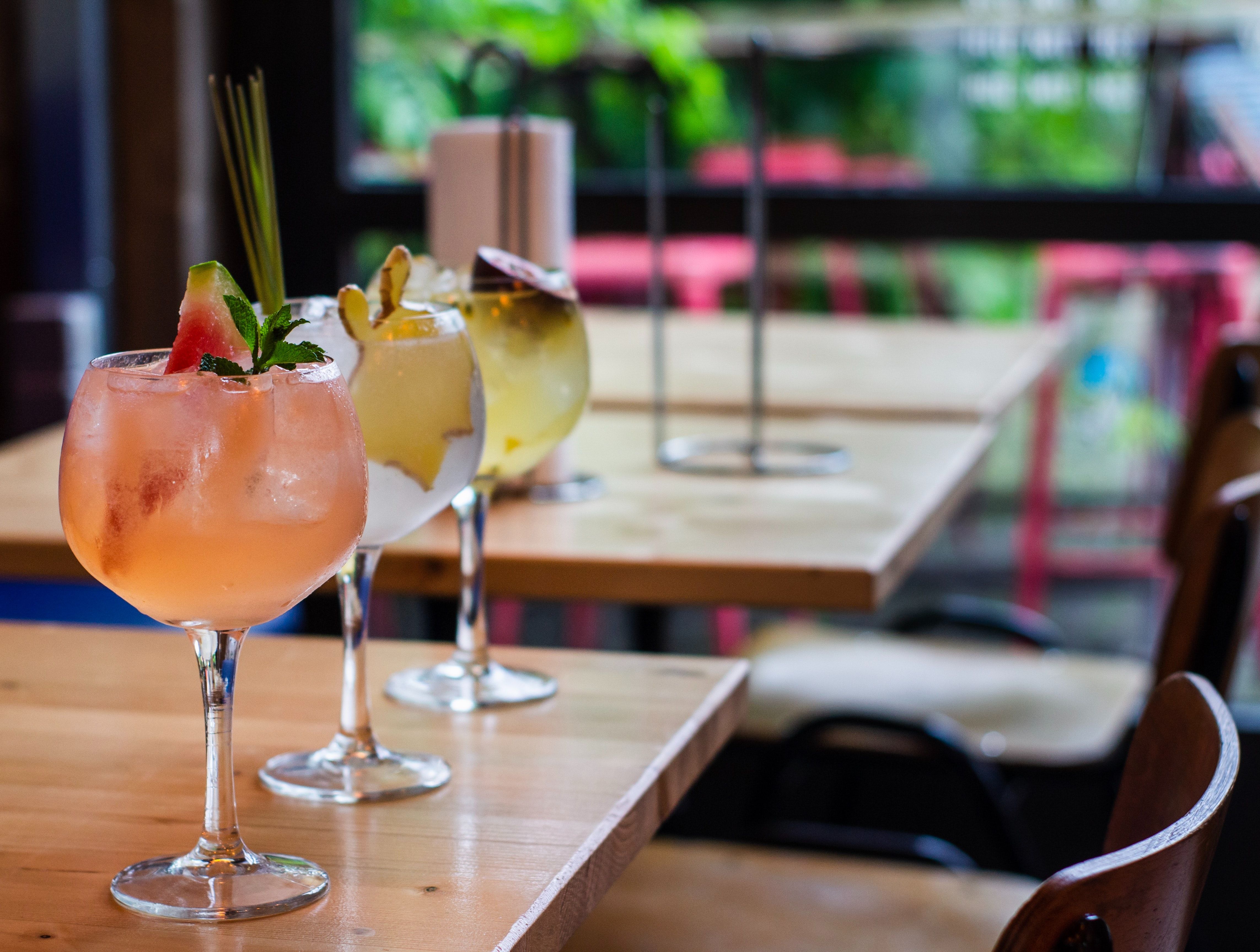 Κοκτέιλ: Τρία πολύχρωμα κοκτέιλ σε ένα ξύλινο τραπέζι σε μοντέρνα μπαρ με φρέσκια υλικά.