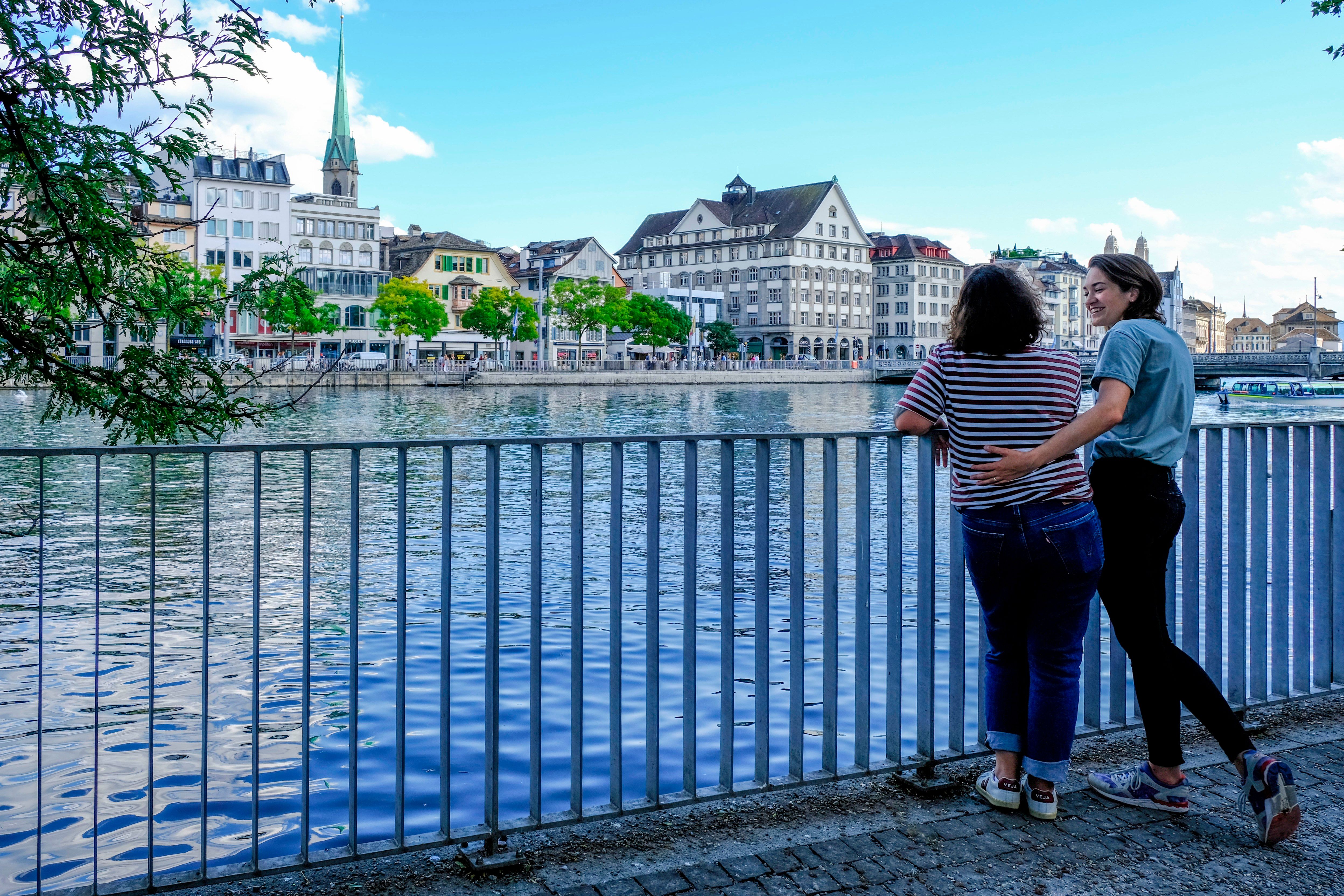 Wanita di Zürich menikmati pemandangan Limmat dengan seni bina dan langit yang cerah.