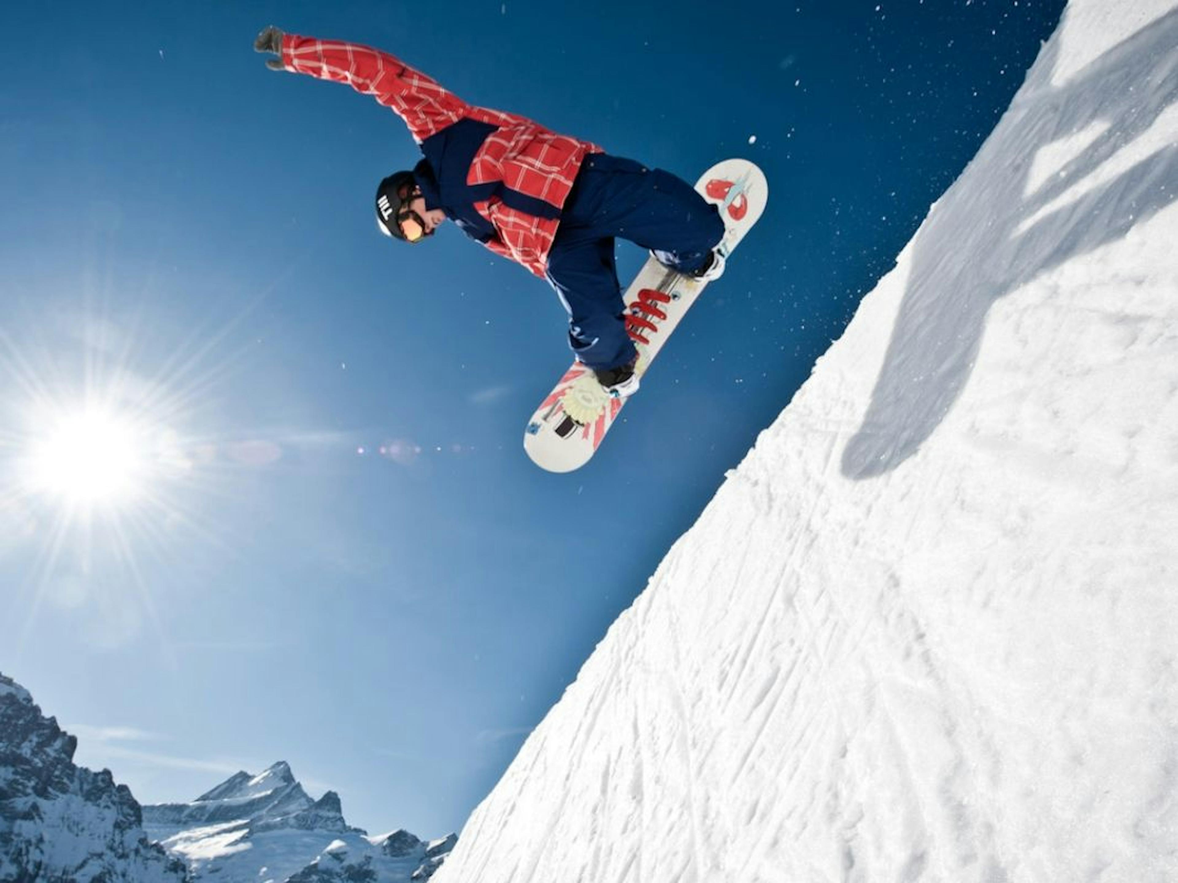 Freestyle Snowboarder springt über eine schneebedeckte Piste in den Alpen.