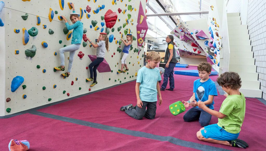 Freiruum Bouldermiljö: Barn som klättrar på inomhusväggar med färgglada grepp och madrasser.