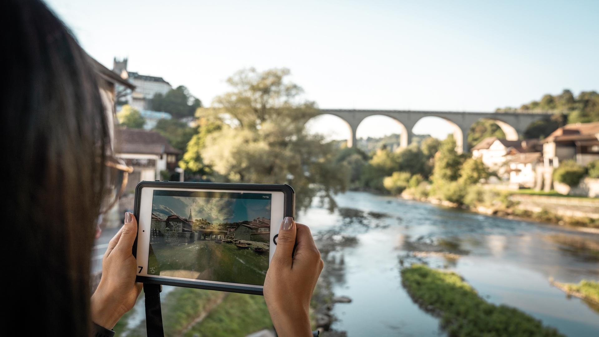 Visita virtual a la ciudad de Fribourg en una tablet junto al río con puente y arquitectura