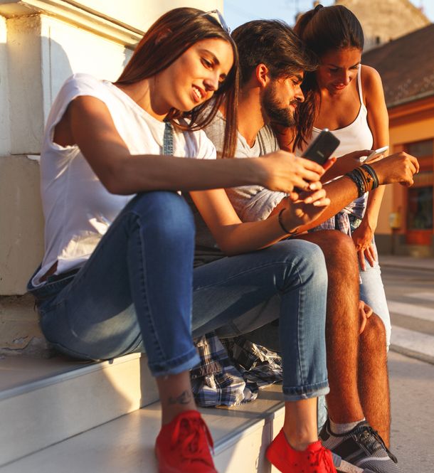 Drei Freunde sitzen auf einer Treppe und schauen auf ihre Handys in Luzern.