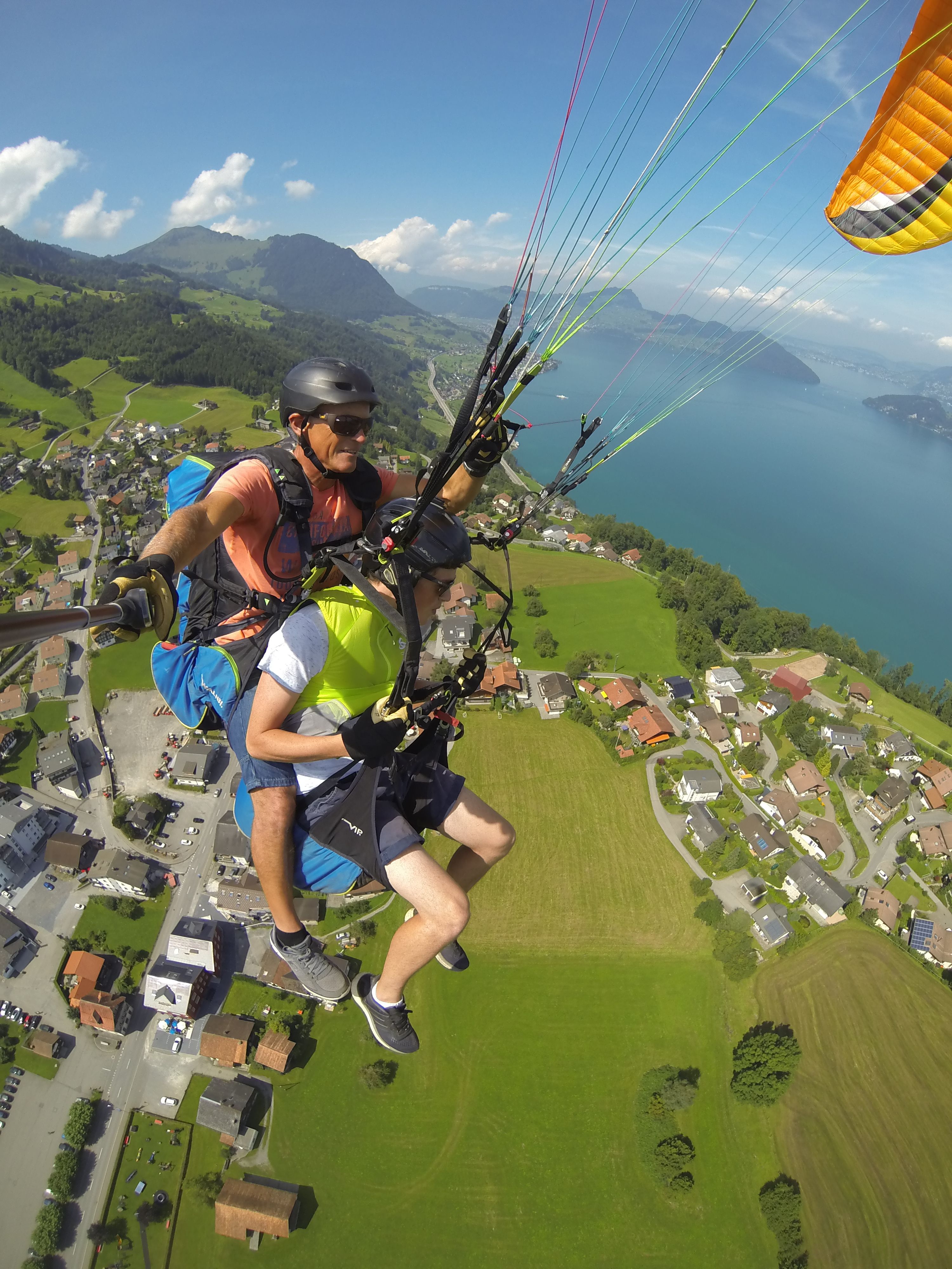 Paragliding ve dvou nad Bodamským jezerem s výhledem na zelené louky a obytné budovy.