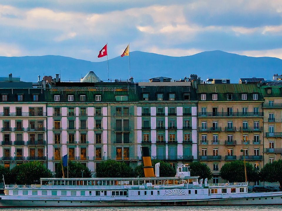 Genewa: Łódka na jeziorze, flaga Szwajcarii, widok na miasto, malowniczy krajobraz.