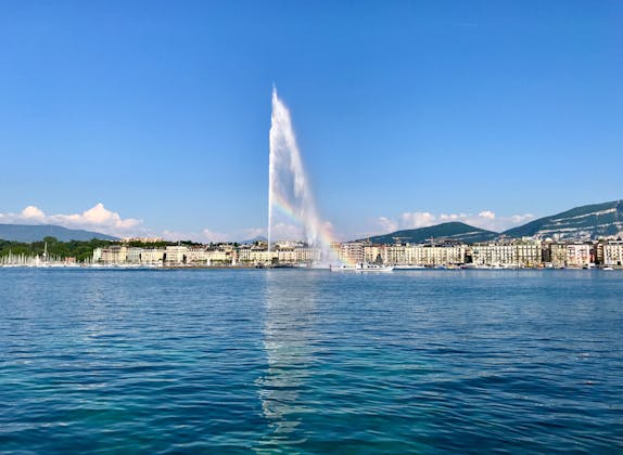 Geneva water feature in the harbor with rainbow, blue sky, and city landscape.