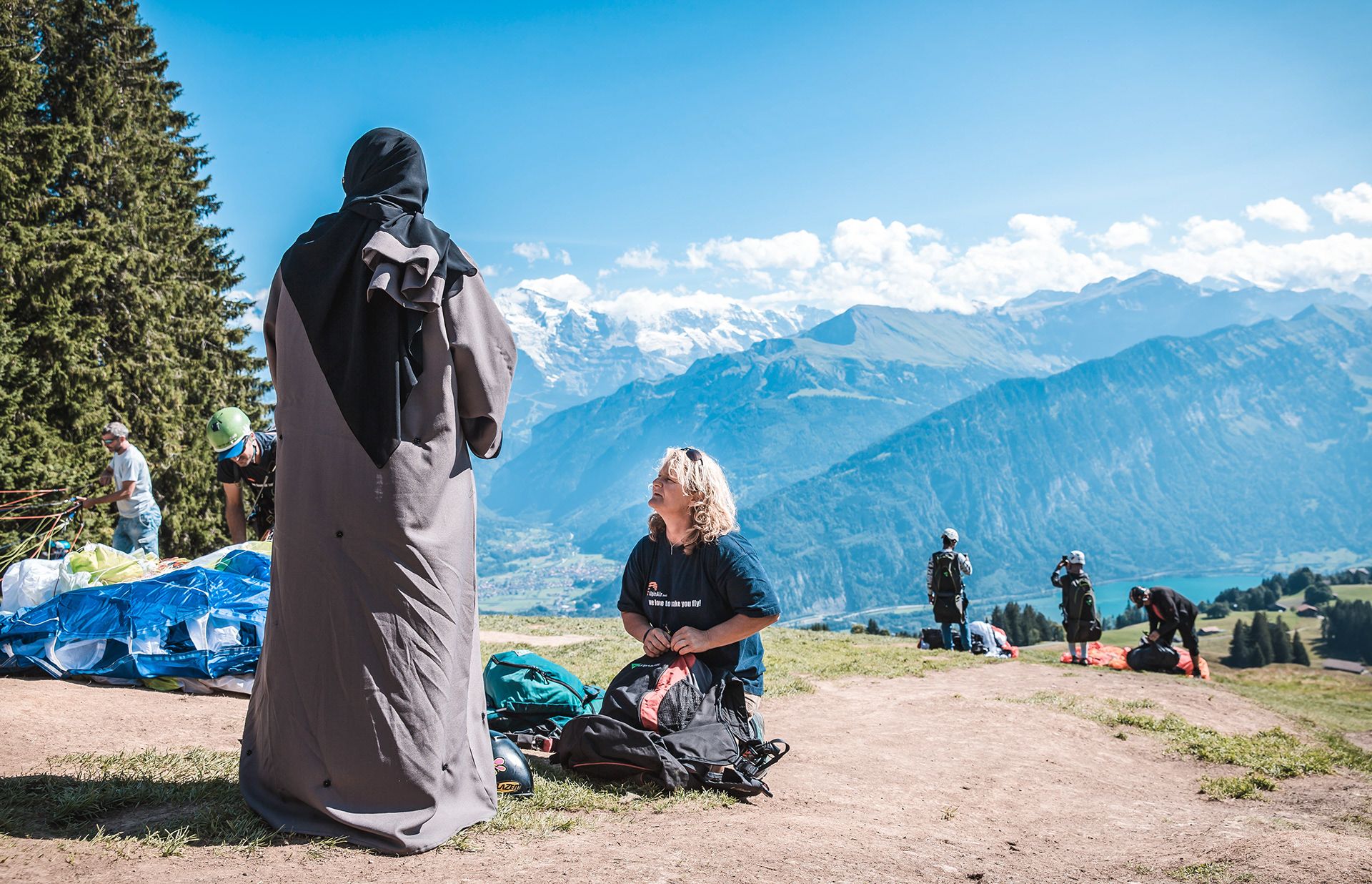 Piloto de parapente prepara o início do voo nos Alpes, dia ensolarado.