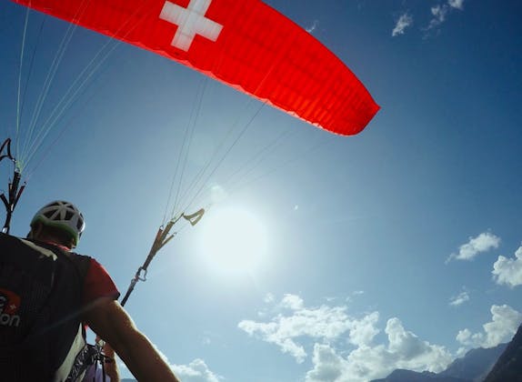 Parapente à Interlaken avec drapeau suisse, ciel bleu et soleil.