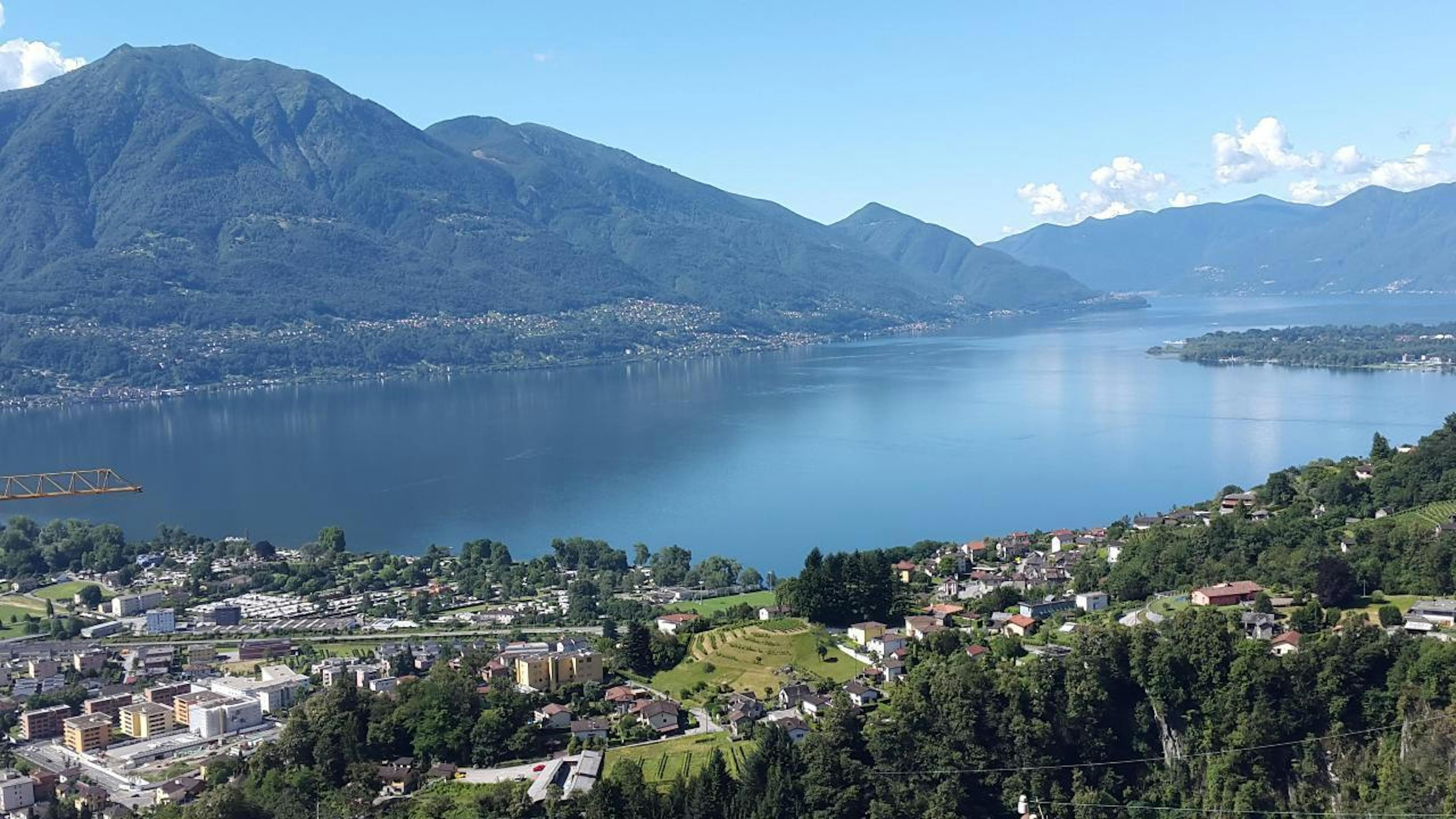 Blick auf den Lago Maggiore von Gordola, Tessin, umgeben von Bergen und Ort