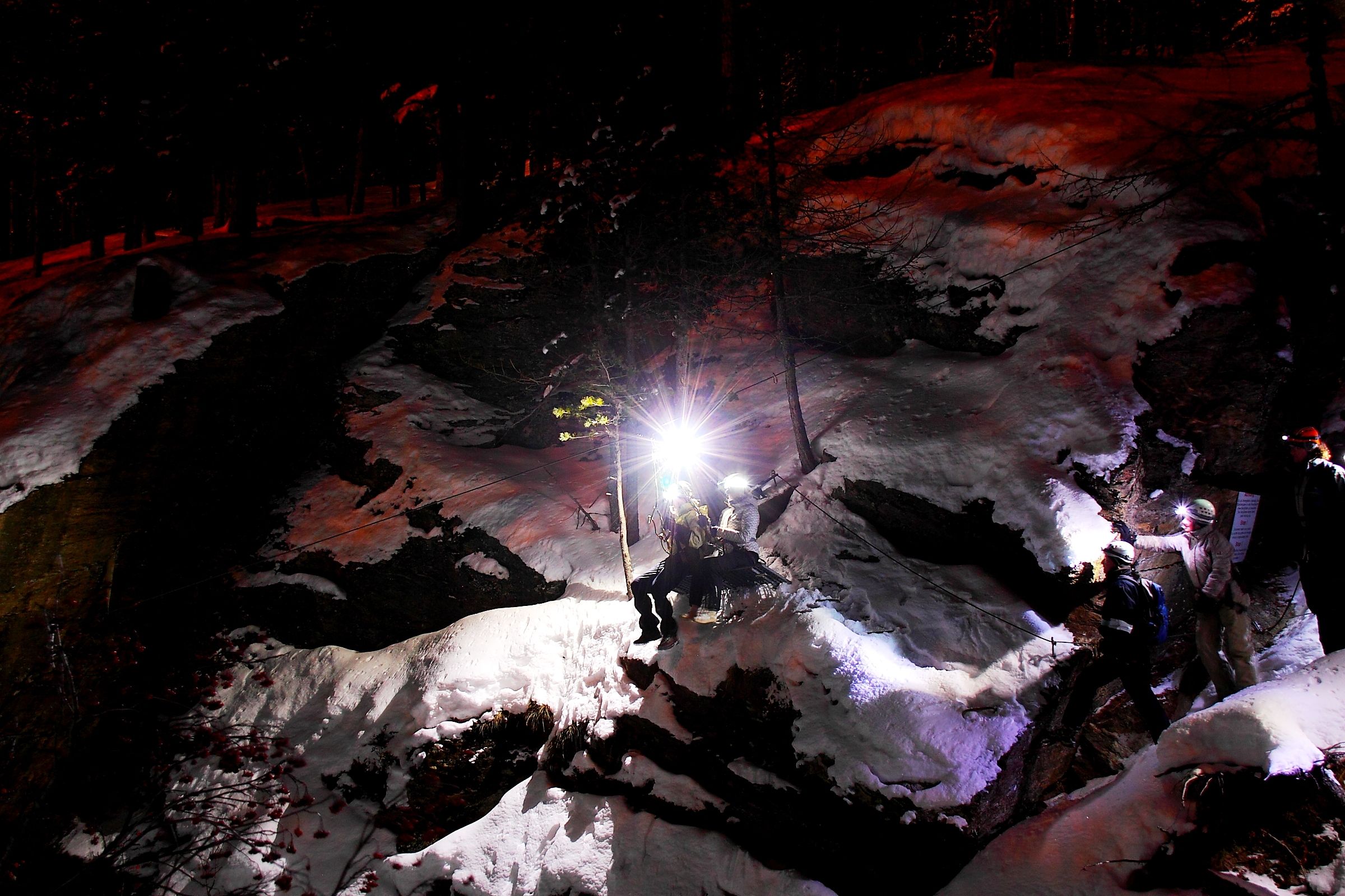 Garganta da Noite: Atmosfera da tarde nos Alpes com rochas cobertas de neve e caminhantes iluminados.