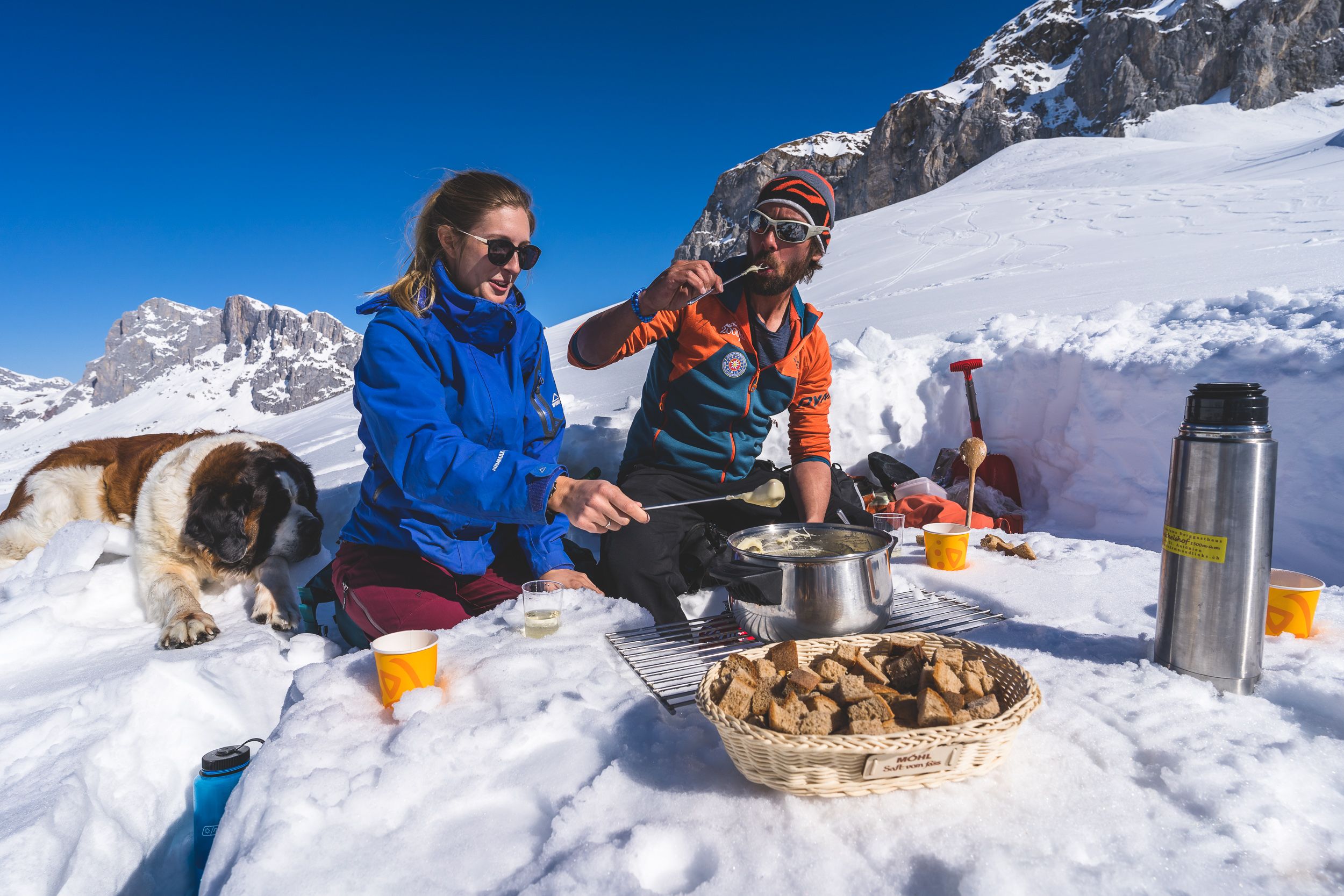 Randonnée en raquettes à neige avec fondue au sommet à St. Antönien, des personnes joyeuses profitent de la fondue dans un paysage enneigé.